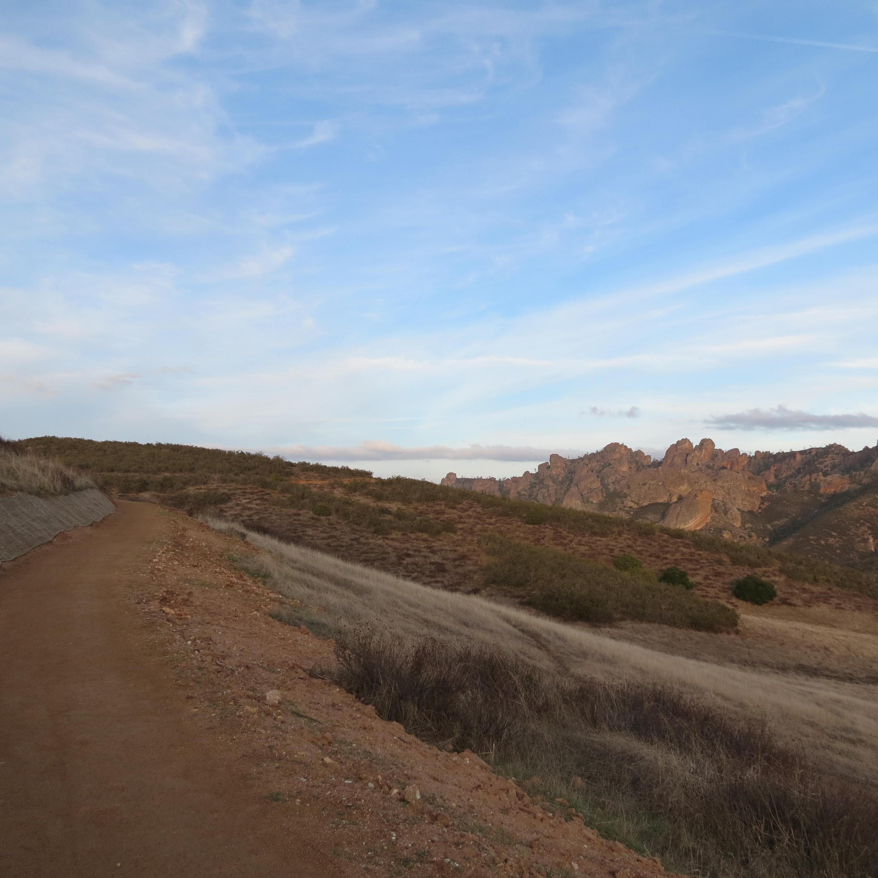 Hard pack dirt trail winding around hillside, large rock spires appearing in the distance.