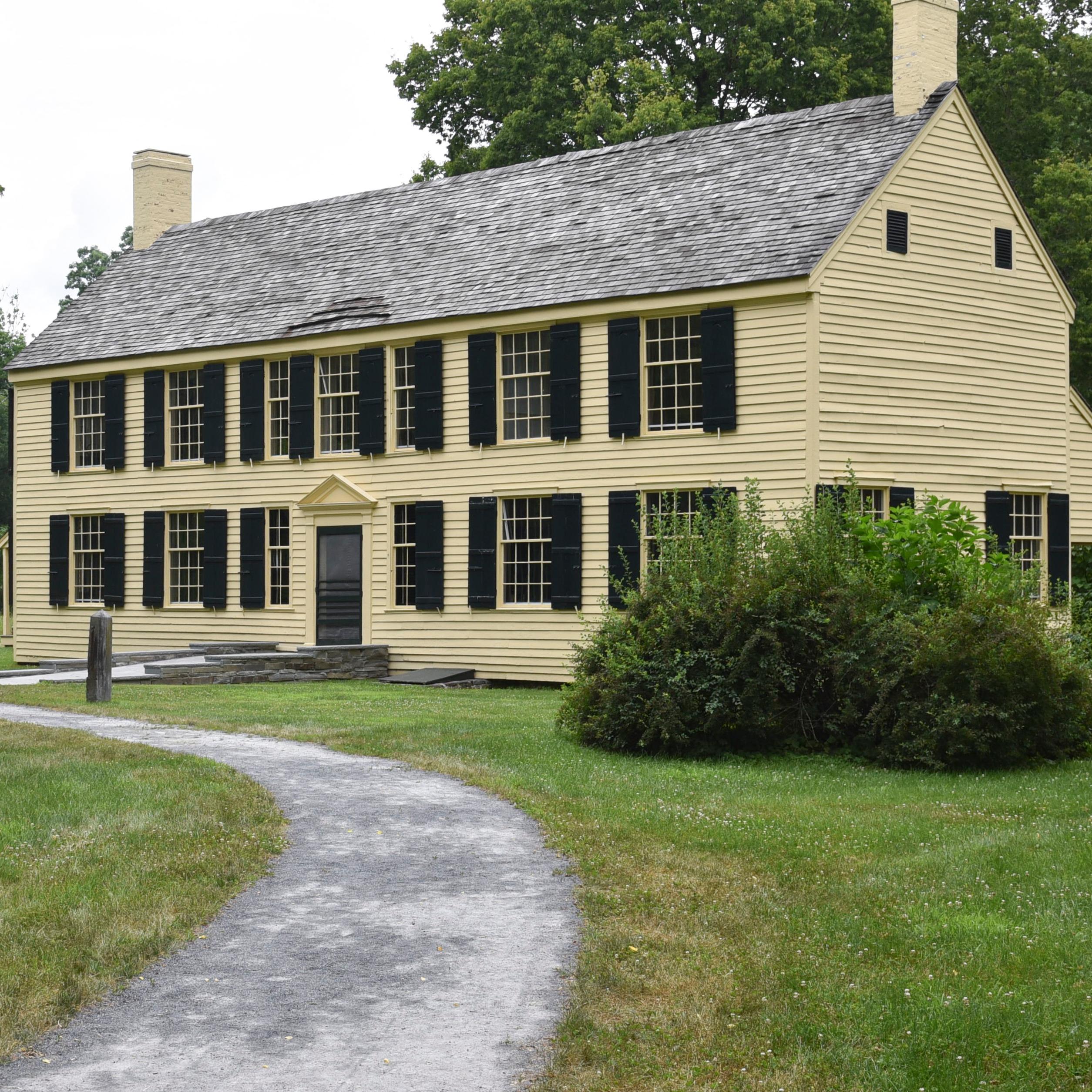 Looking down a path to a two story yellow house