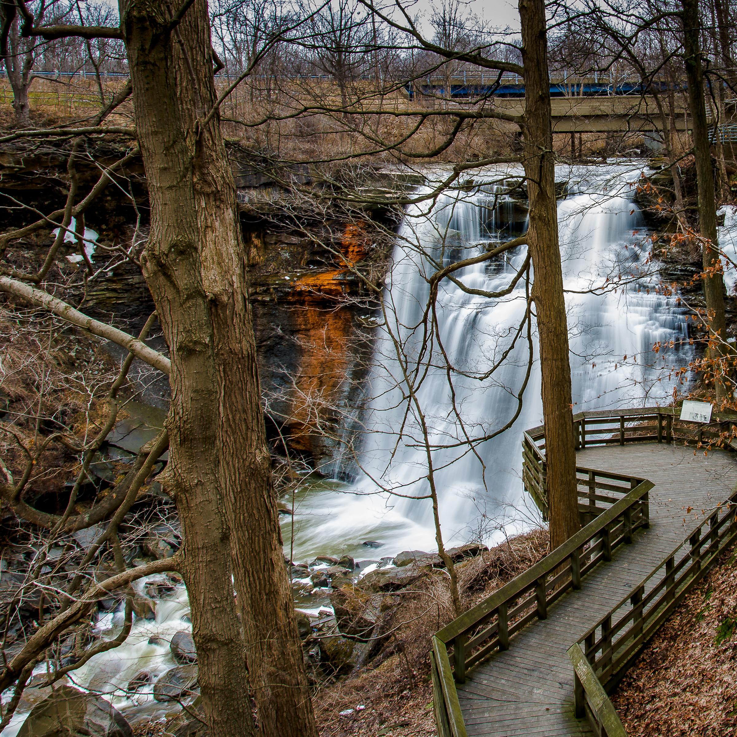 View down through bare trees at a deck overlooking a waterfall cascading into a gorge.
