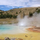Steam rises from a blue-, yellow-, and orange-colored hot spring.