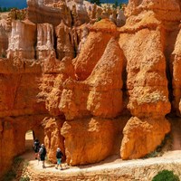 Hikers walk along a trail towards an open archway in the red rock
