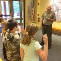 children taking a pledge in the foreground with a Park Ranger standing in the background.