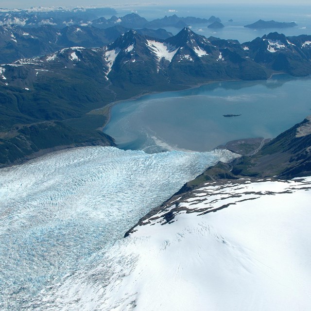 Snowfield and glacier in the foreground, leading to the ocean surrounded by mountains. 