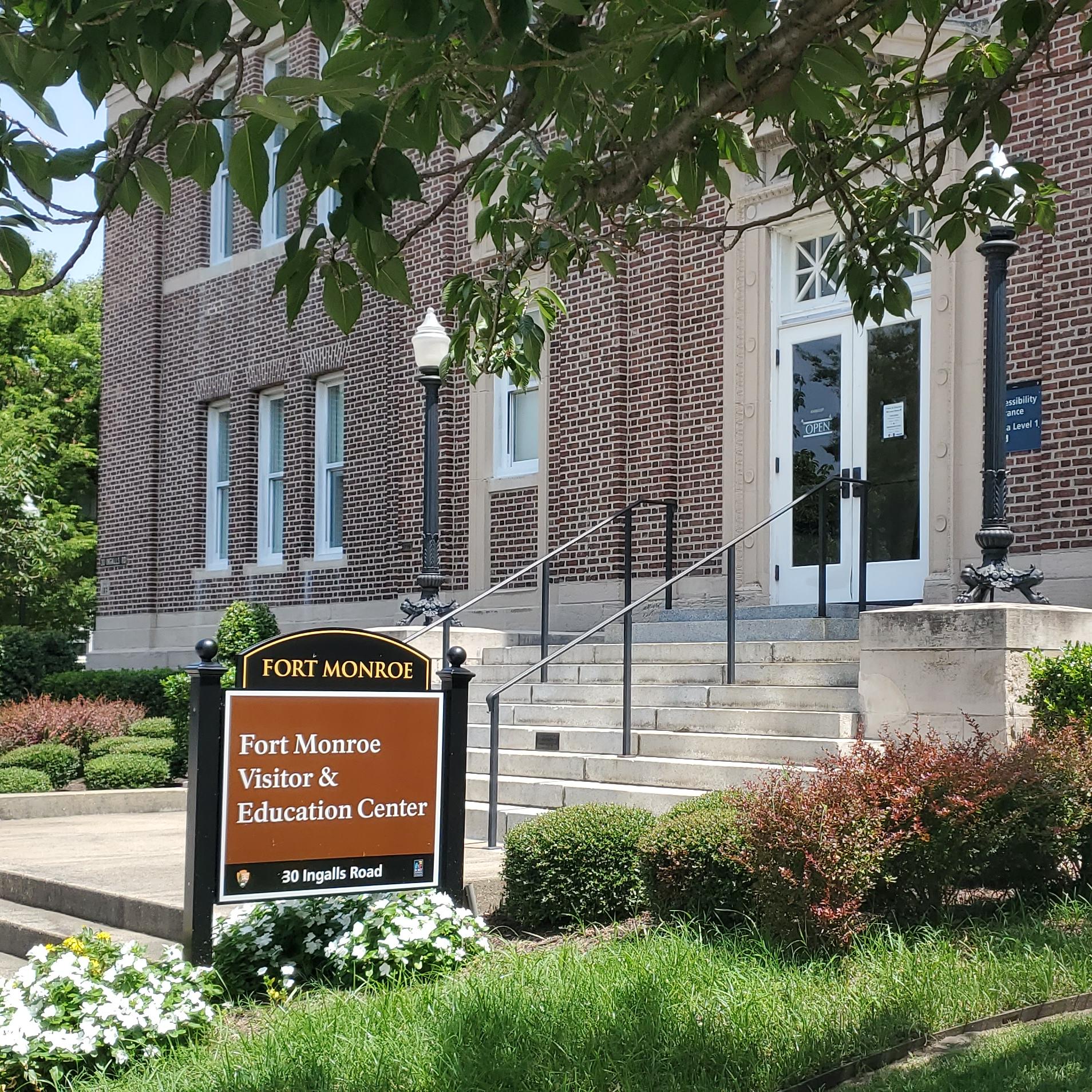 Signs in front of a brick Beaux-Arts style building state that the visitor center is open. 