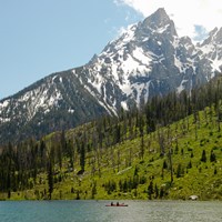 A kayak floats in a turquoise lake at the base of jagged mountain peaks.