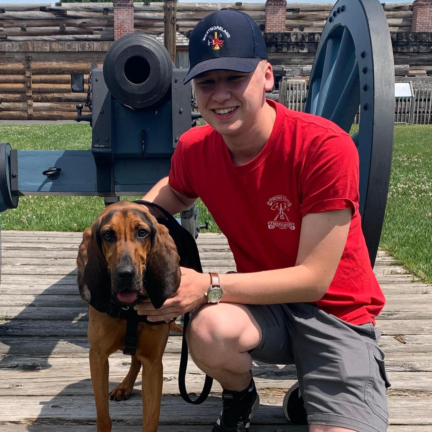 A sweet doggy stands on a leash with his person in front of a cannon.