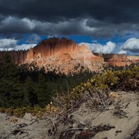 A large formation of red rock partially in shadow with threatening storm clouds above it