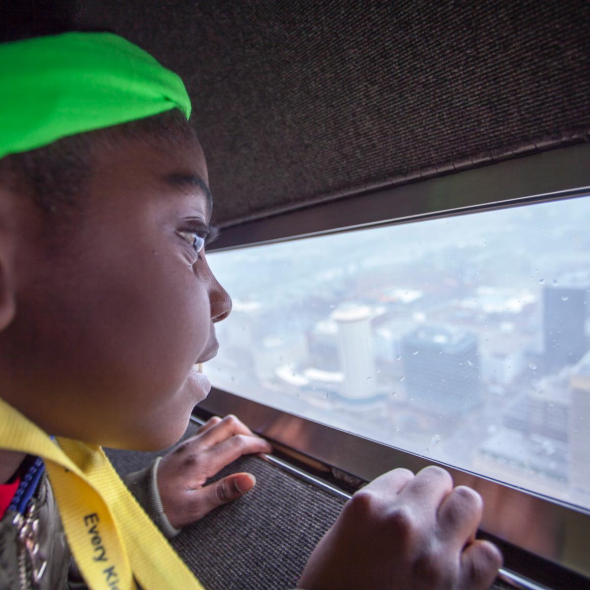 a young African-American girl looks out of the window of the Arch onto the city below