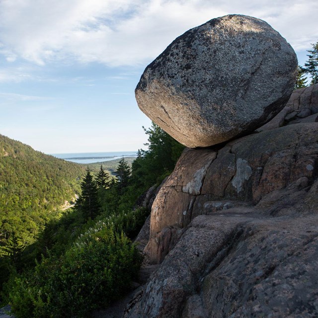 a round boulder perches on the side of a mountain