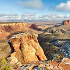 red sandstone cliffs frame rolling green canyon bottoms, snow in shade, low clouds in distance