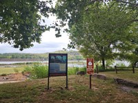 Trail of Tears exhibit and mileage sign with river and lock and dam behind.