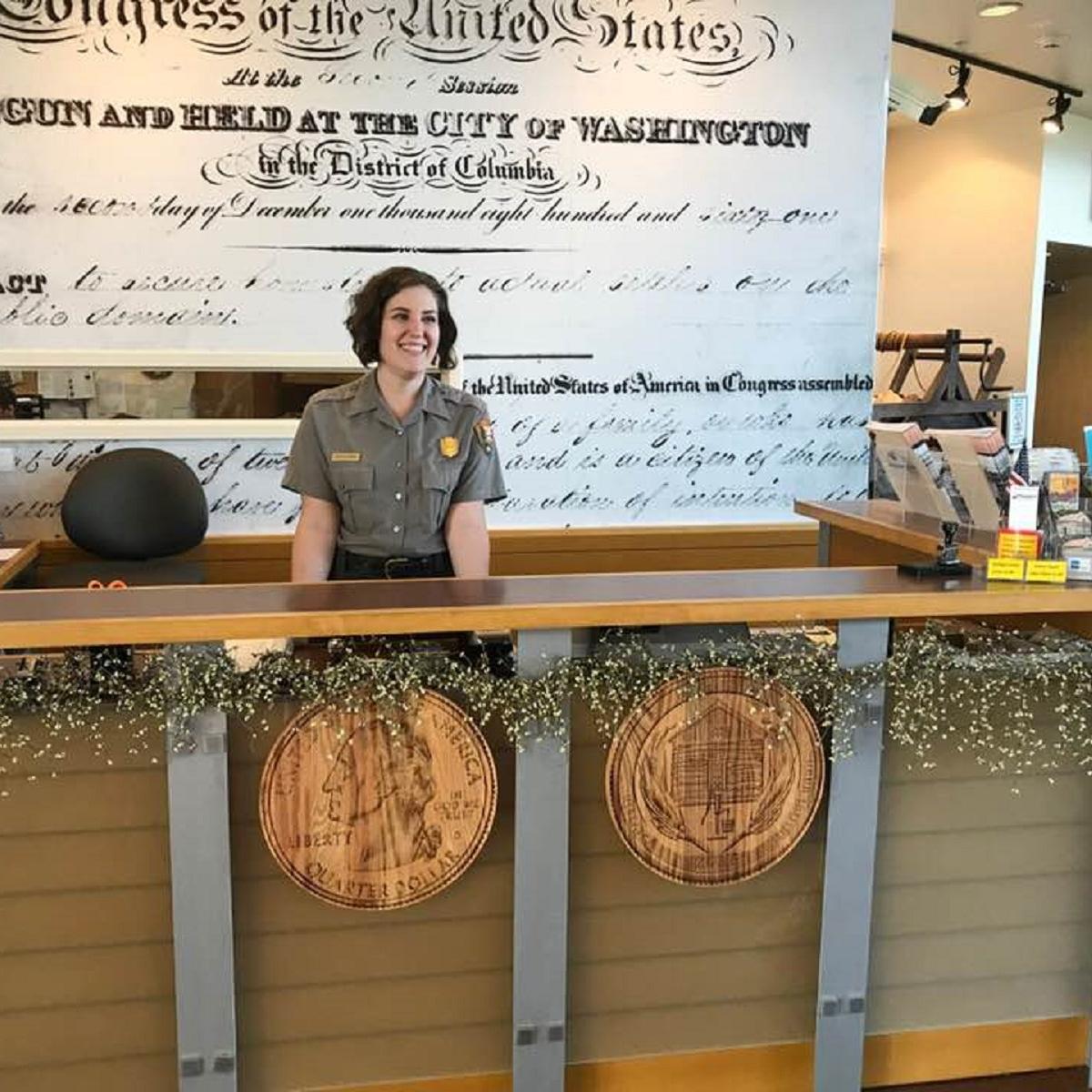A ranger smiles standing behind an information desk.