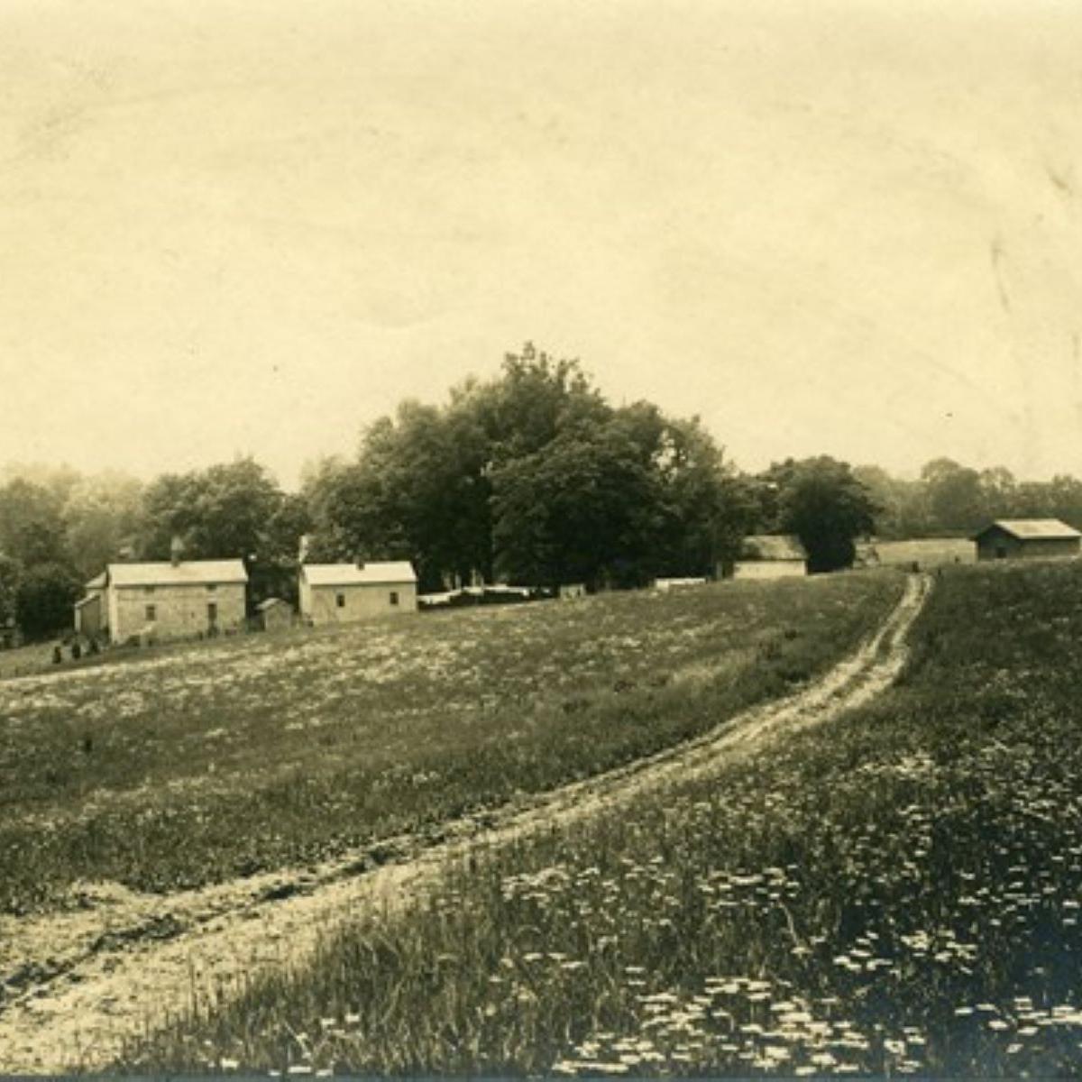 A black and white historic photograph of the farm side structures.