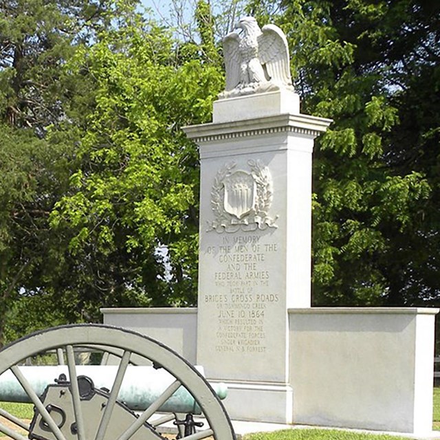 An artillery canon sits next to a white stone monument