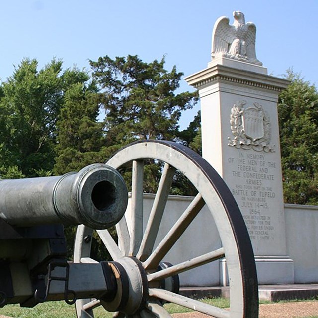 Field gun sitting on manicured lawn in front of white stone monument