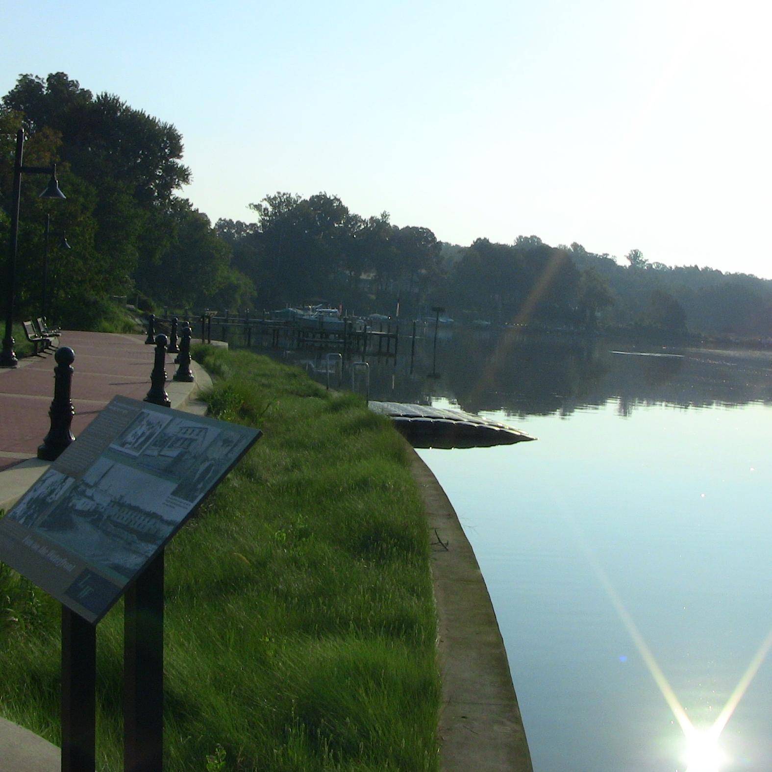 a curving concrete pathway and green border along water with a sloping kayak launch