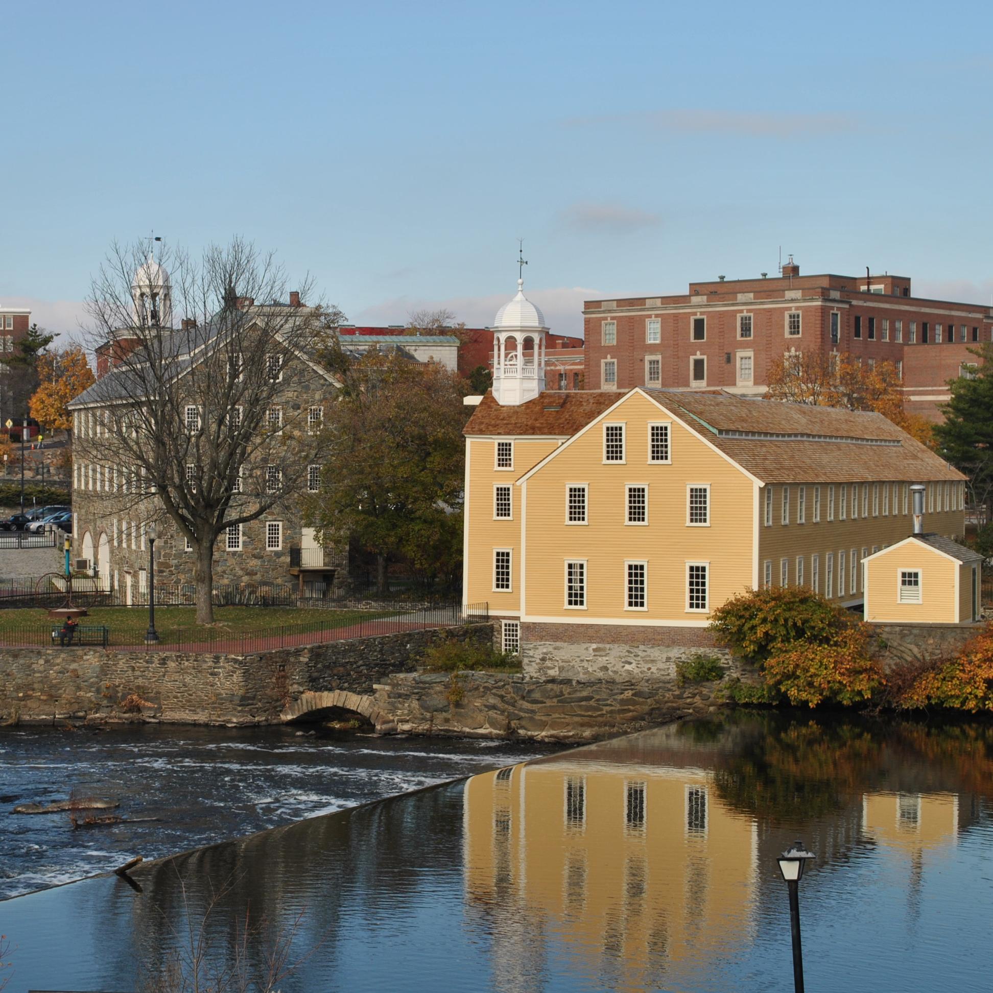 River in foreground with yellow mill and other buildings in distance