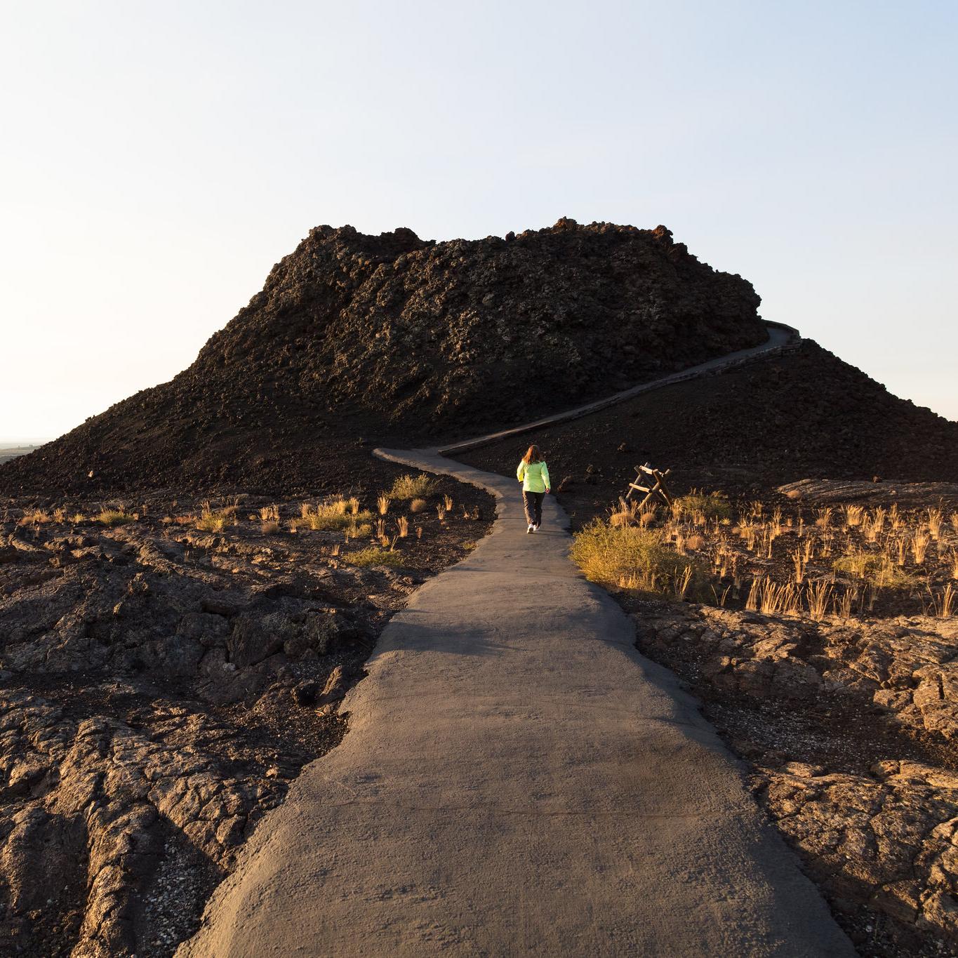 a person walking on a paved path up to a small volcanic cone