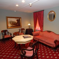 A small red-carpeted room with faux marble table, red upholstered chairs and sofa, and red curtains.