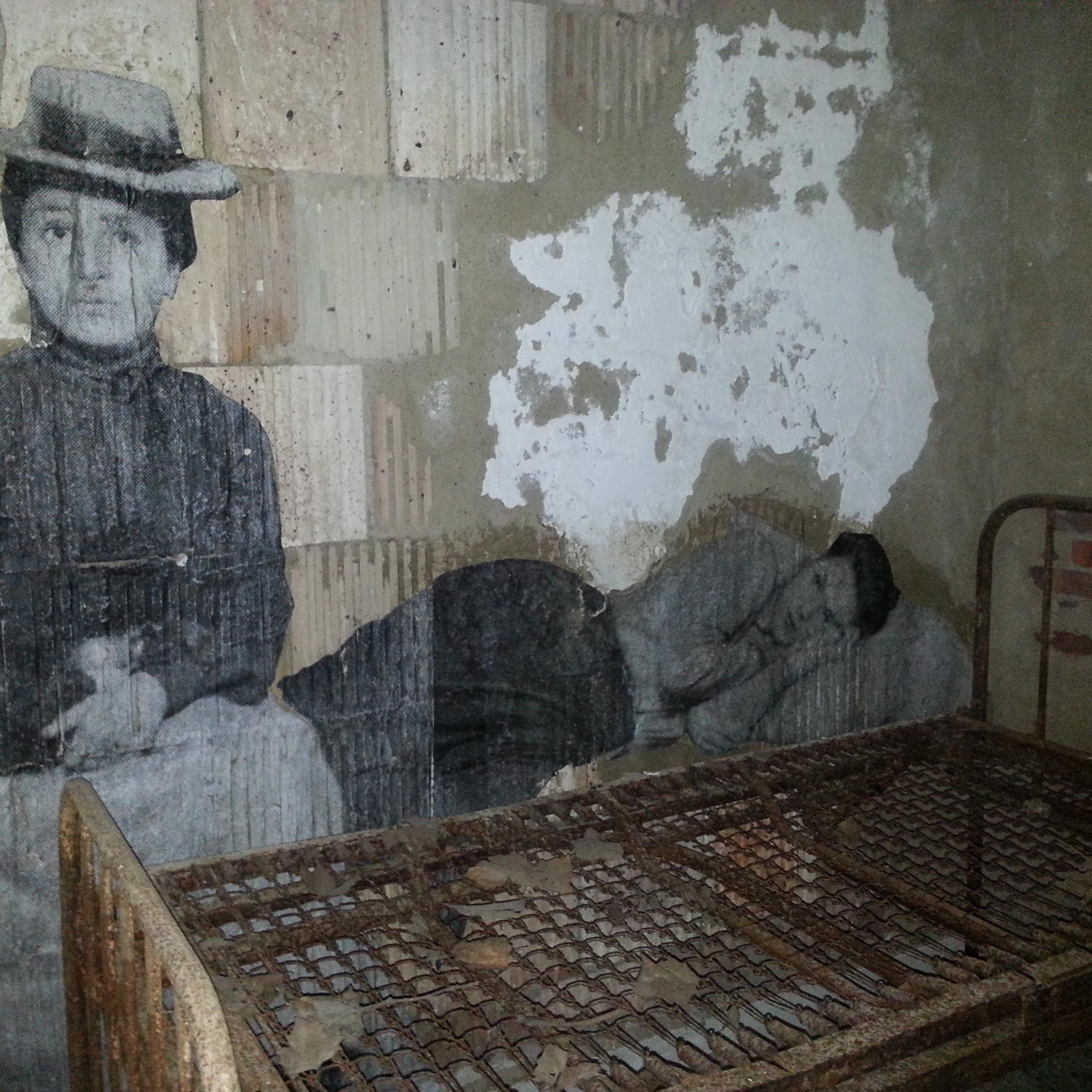 A black and white photograph of an immigrant sitting near an old bed rack in the hospital.