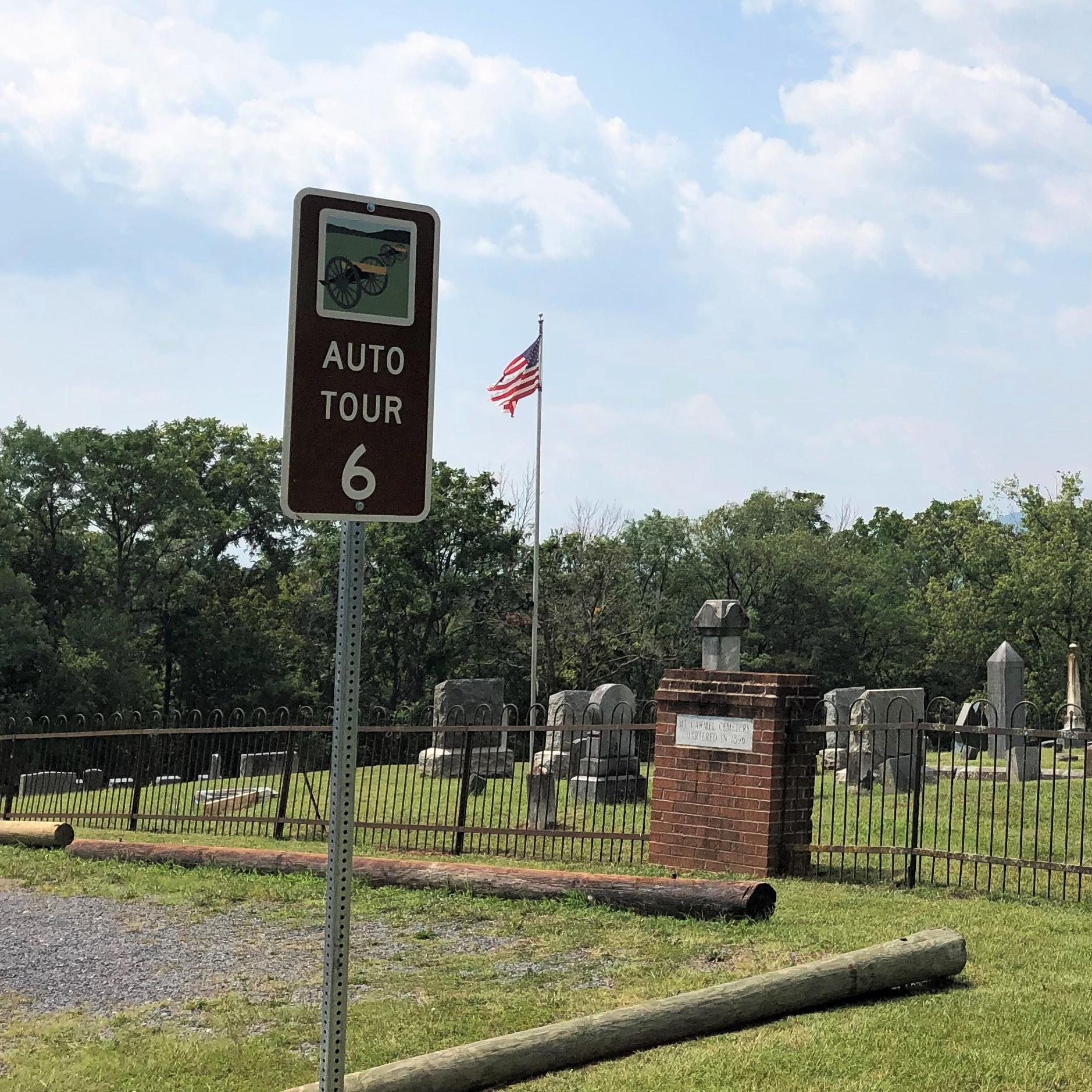 A road sign labeled auto tour 6 marks a tour stop and exhibit by a cemetery.