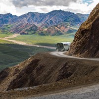 a green colored bus traveling a dirt road on a mountainside