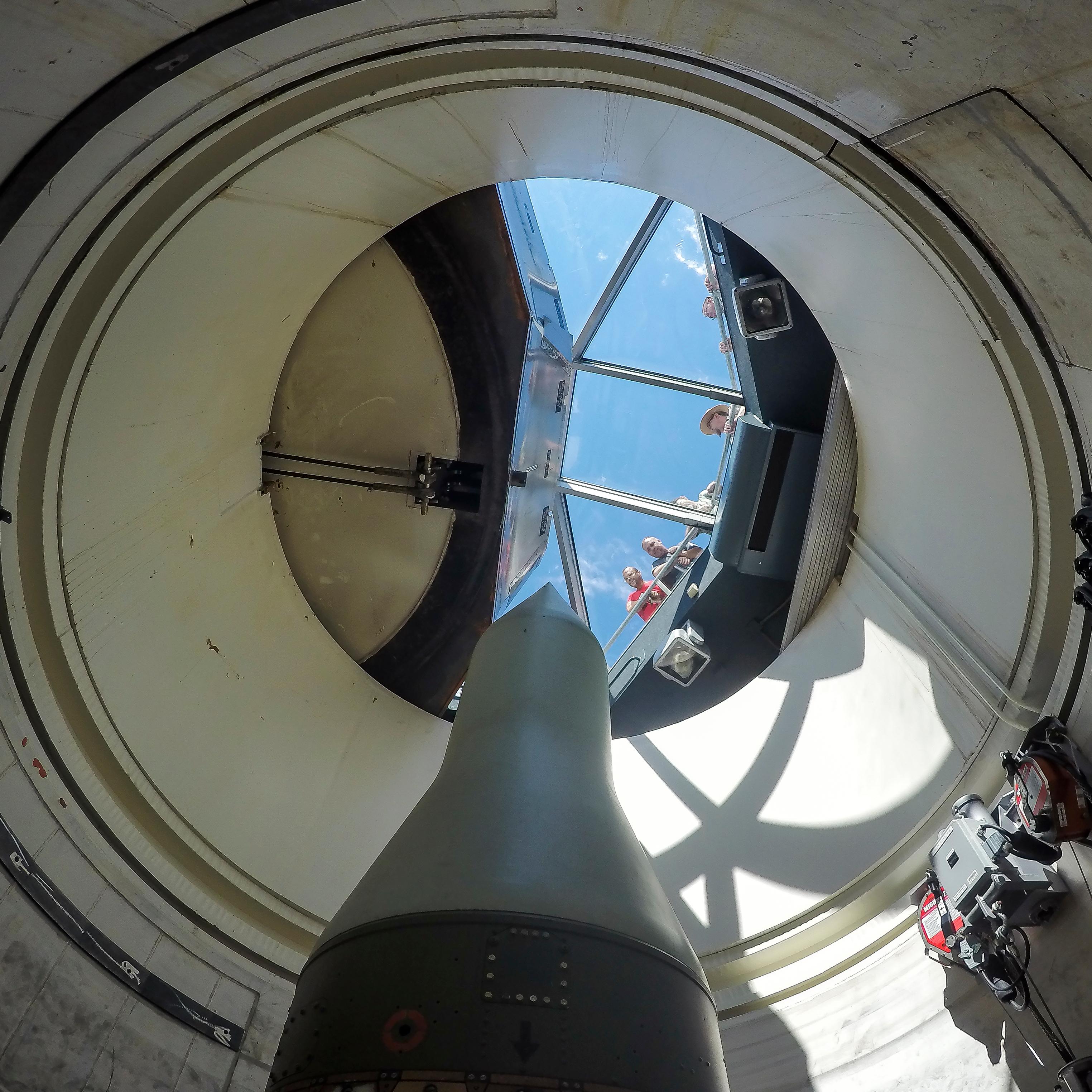 Park ranger and visitors look through a glass barrier at a missile standing in a missile silo
