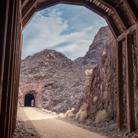 A tunnel constructed of wood beams looking out down a trail towards another tunnel.