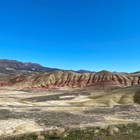 Red and yellow striped hills with tan grasses in the foreground and blue skies.