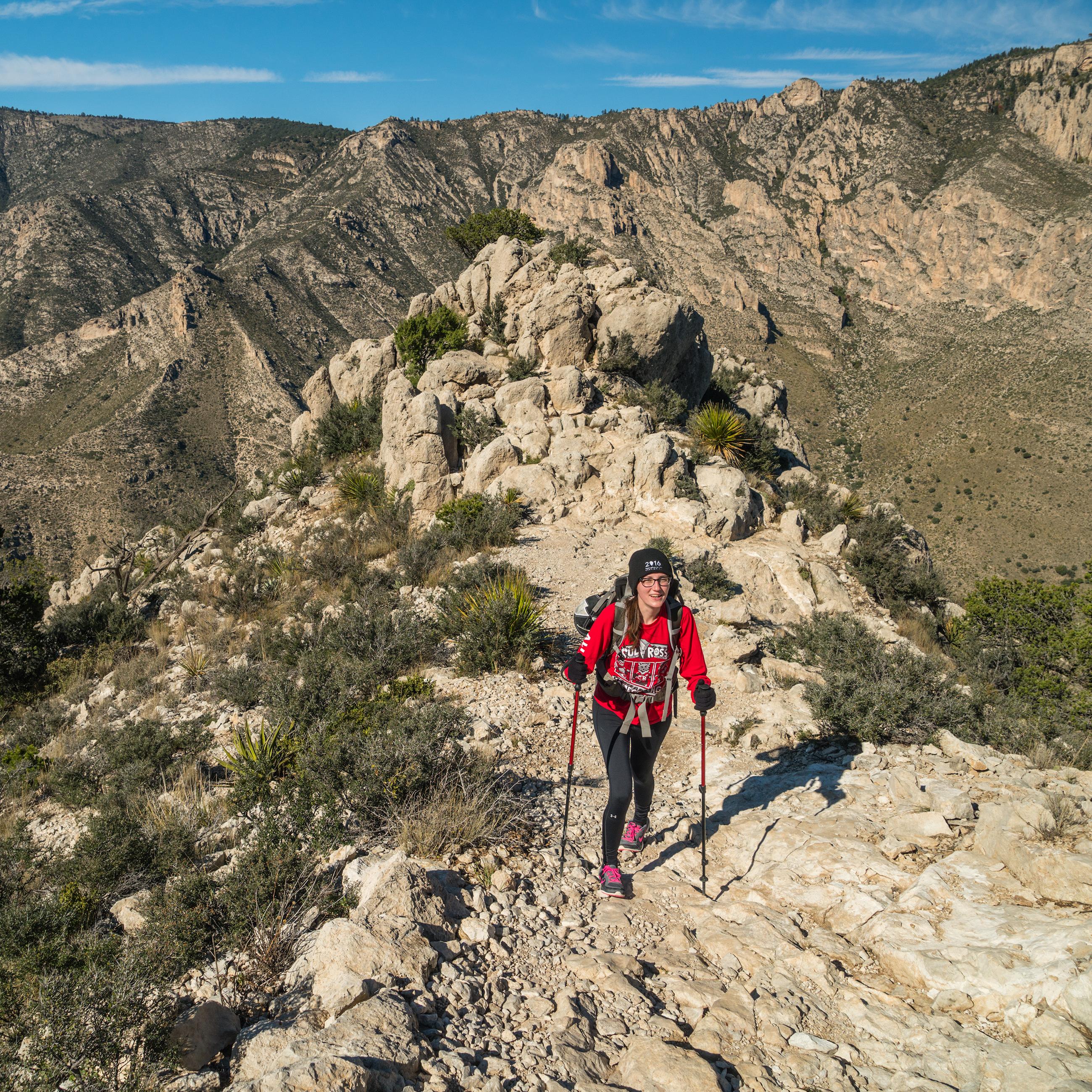 a woman with hiking poles ascents a mountain trail