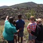 two adults pointing at a large cinder cone with three children