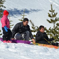 a family preparing to sled down a snowy hill
