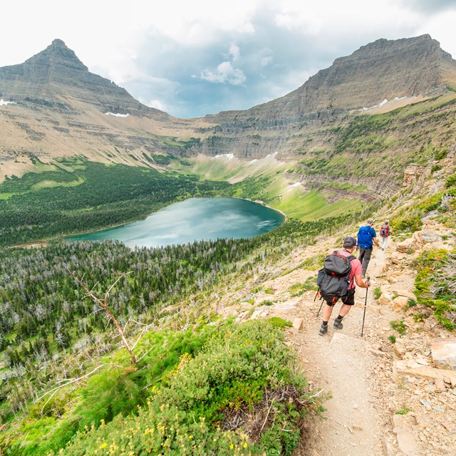 hikers on a trail near a clear blue lake