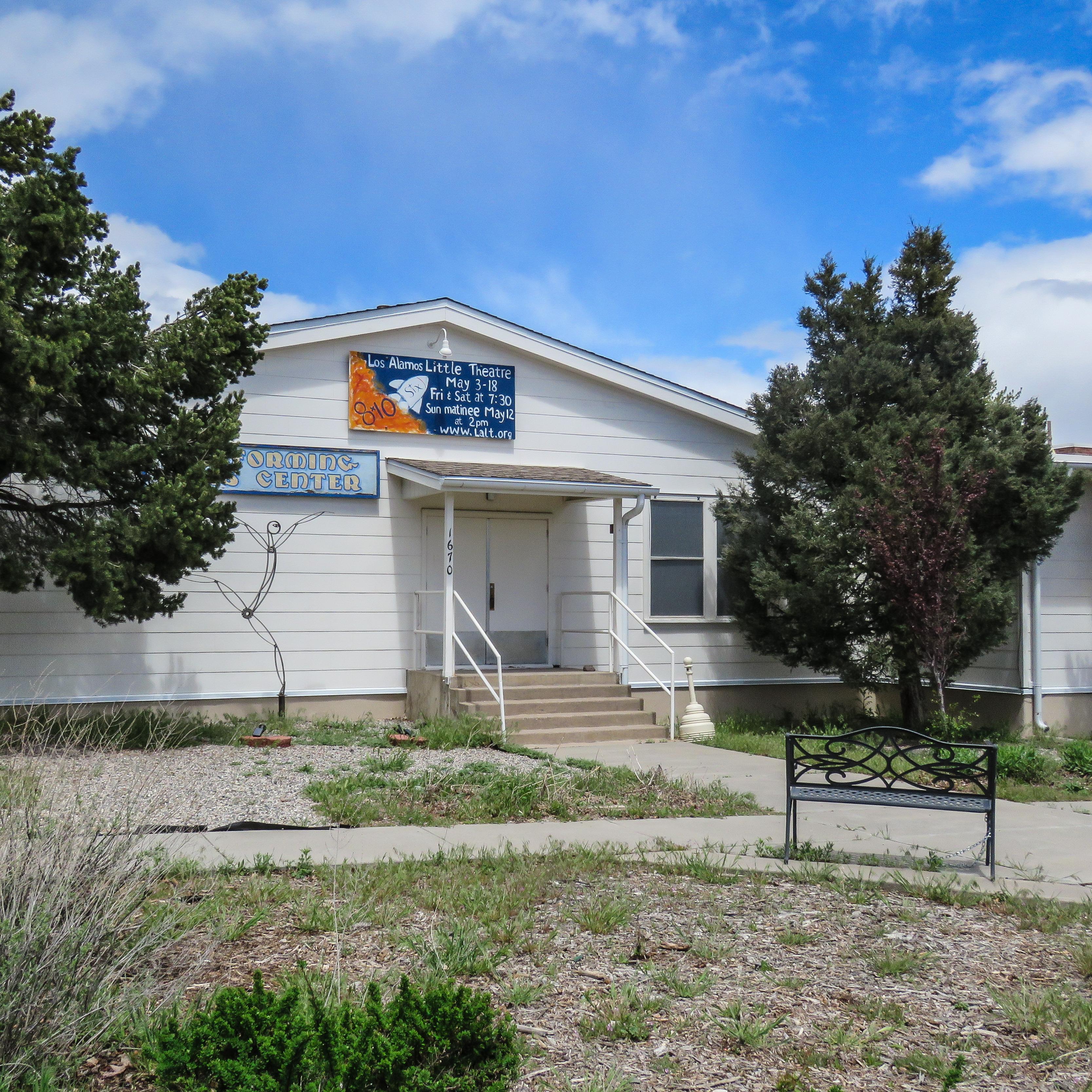 A wooden, white building with a blue and orange sign with white text.