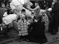 Japanese women and children shown with luggage and are waiting on a train.
