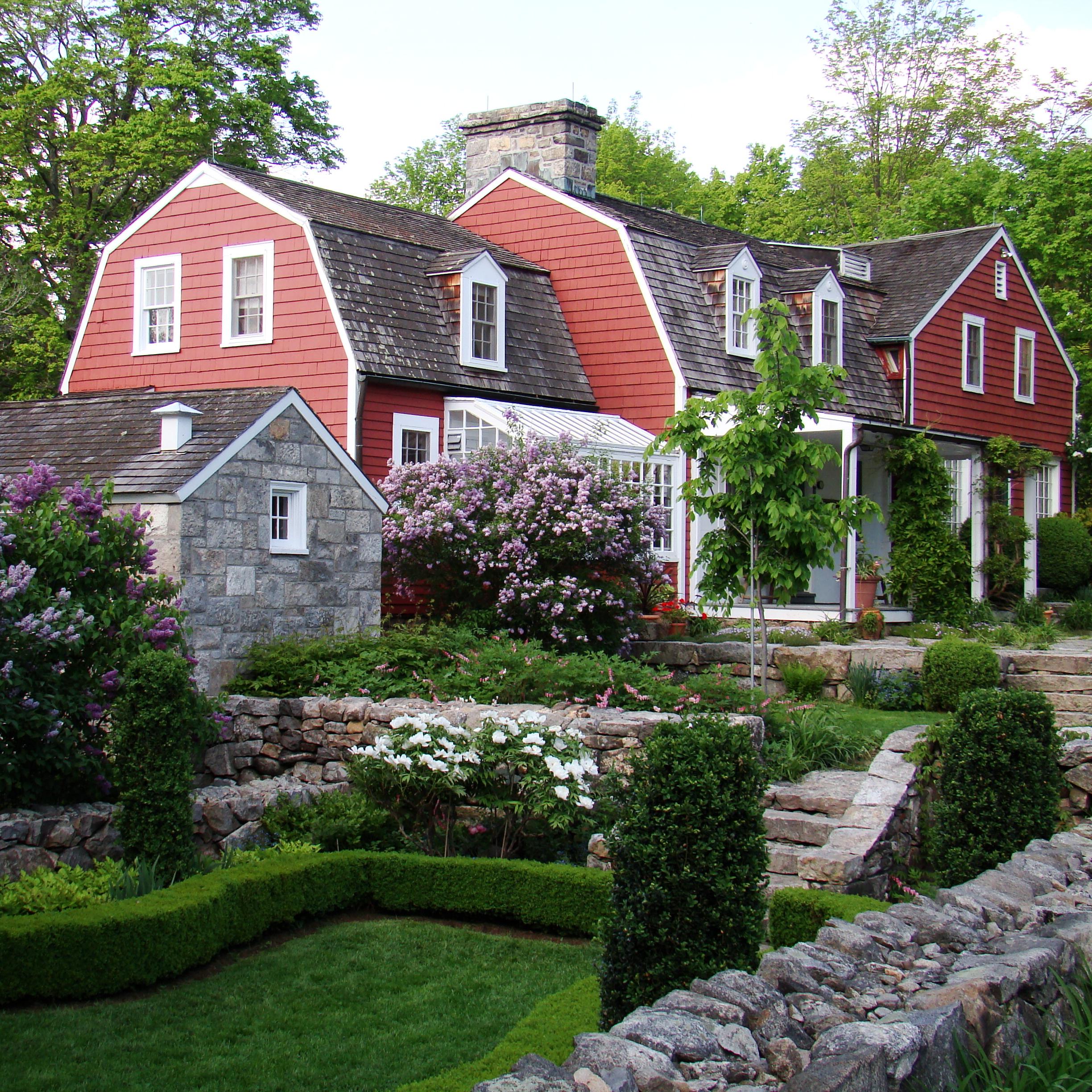 A red house with a stone wall and flowers around it.