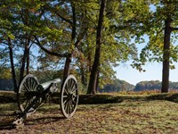 A cannon perched on a knoll overlooking a wide open field.