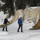 Two skiers traveling in front of a orange-colored hot spring terrace.