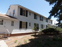 A long, two story white wood-sided building sits on a grass lawn