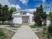 At the end of a wide sidewalk, a white sided building with double doors sits under a cloudy sky.