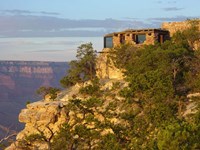 A rustic stone building with large windows on the edge of a cliff overlooking a canyon.
