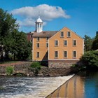 Yellow mill on banks of Blackstone River with dam and waterfall in the foreground