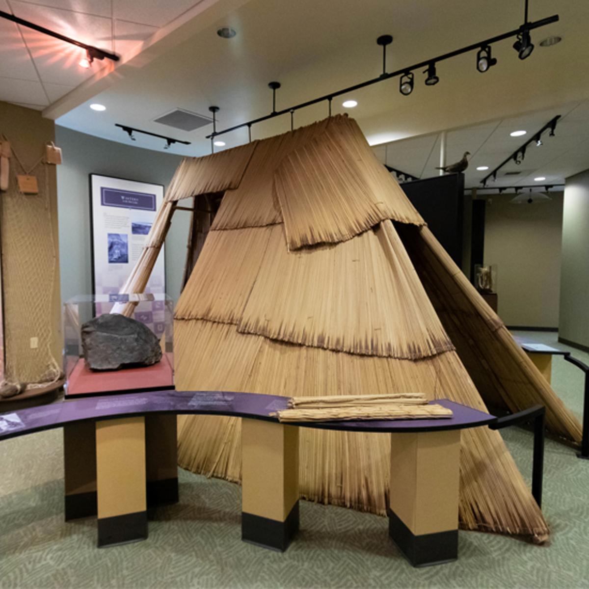 A color photo of an inside room with a windy table. There’s a structure made from organic mats.