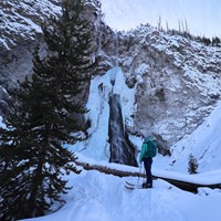 A skier looks up at the ice formations surrounding a frozen waterfall.