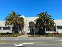 Large two story building with multiple windows and two palm trees in front.