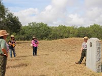 Visitors stand looking at a park ranger standing next to a historical marker.