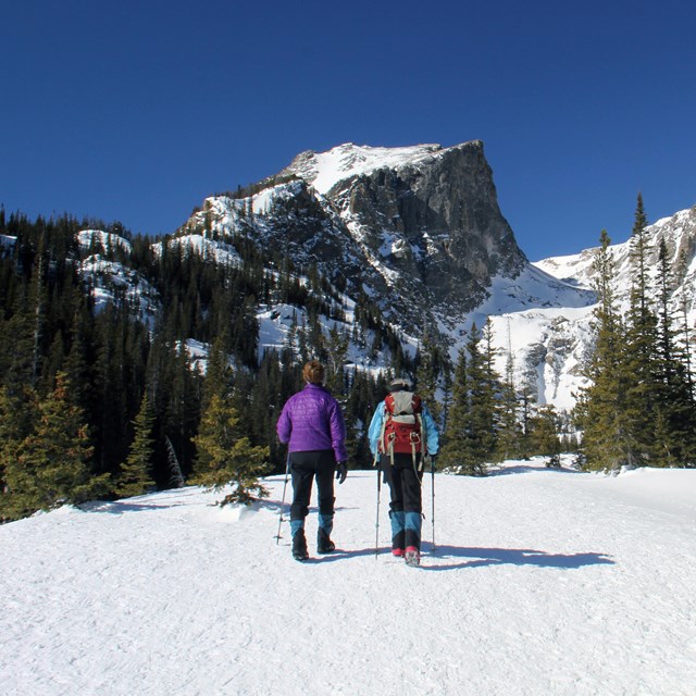 Two people are snowshoeing on a trail in RMNP