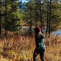 A female hiker walks along a wooded trail by a river.