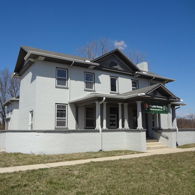 A large gray house with several windows under a blue sky with green grass in the yard