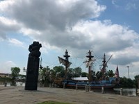 A wooden ship sails past a monument.